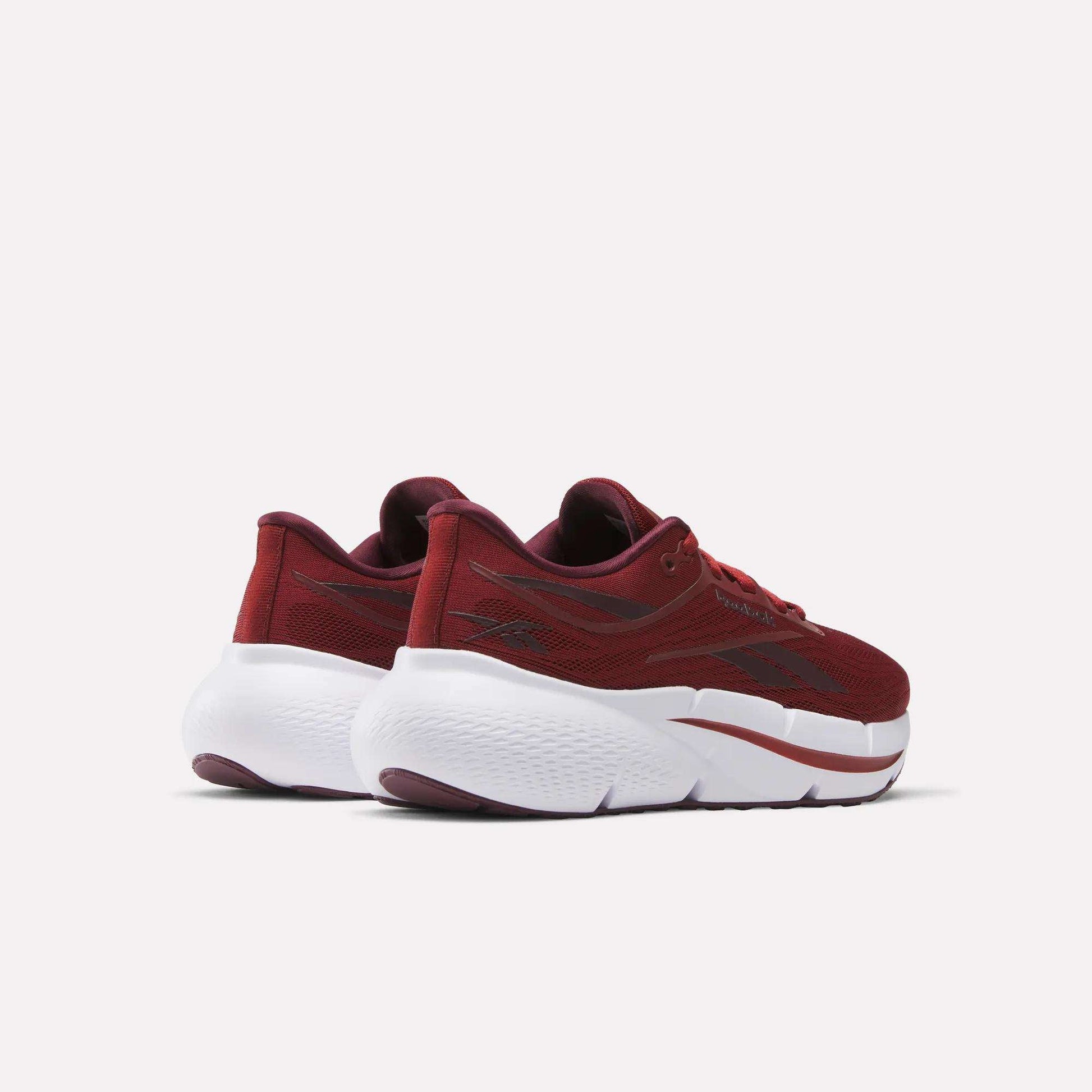 A pair of Women's Zignition Running Shoes by Reebok in maroon, featuring mesh uppers and chunky white soles, is shown from a rear side angle against a plain white background.