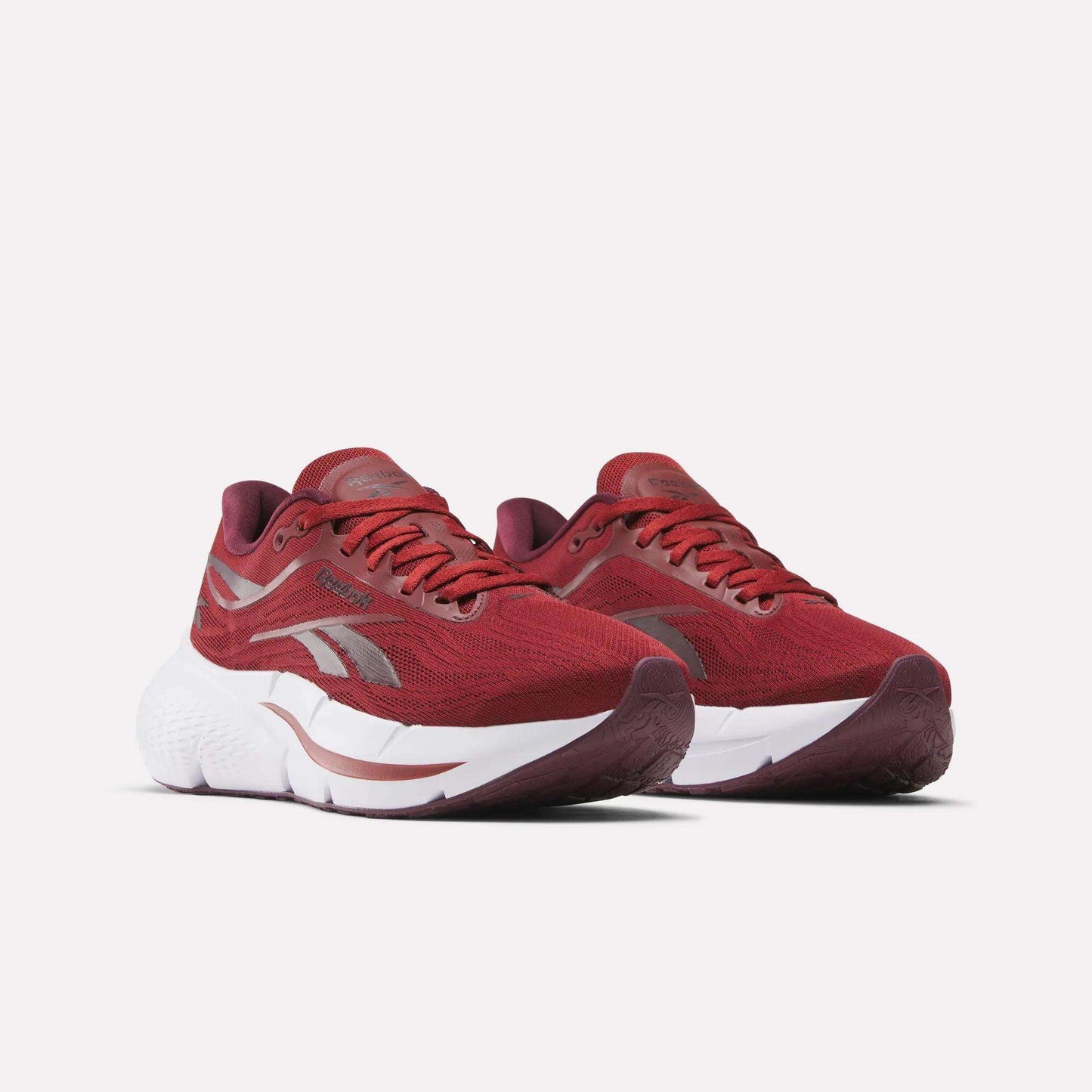 A pair of Reebok Women's Zignition Running Shoes in red with cushioned white midsoles and silver accents are placed side by side on a plain white background.