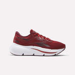 A side view of Reebok Women's Zignition Running Shoes in red, featuring a white sculpted sole and grey brand accents, displayed on a plain white background. Ideal for runners seeking cushioned comfort.