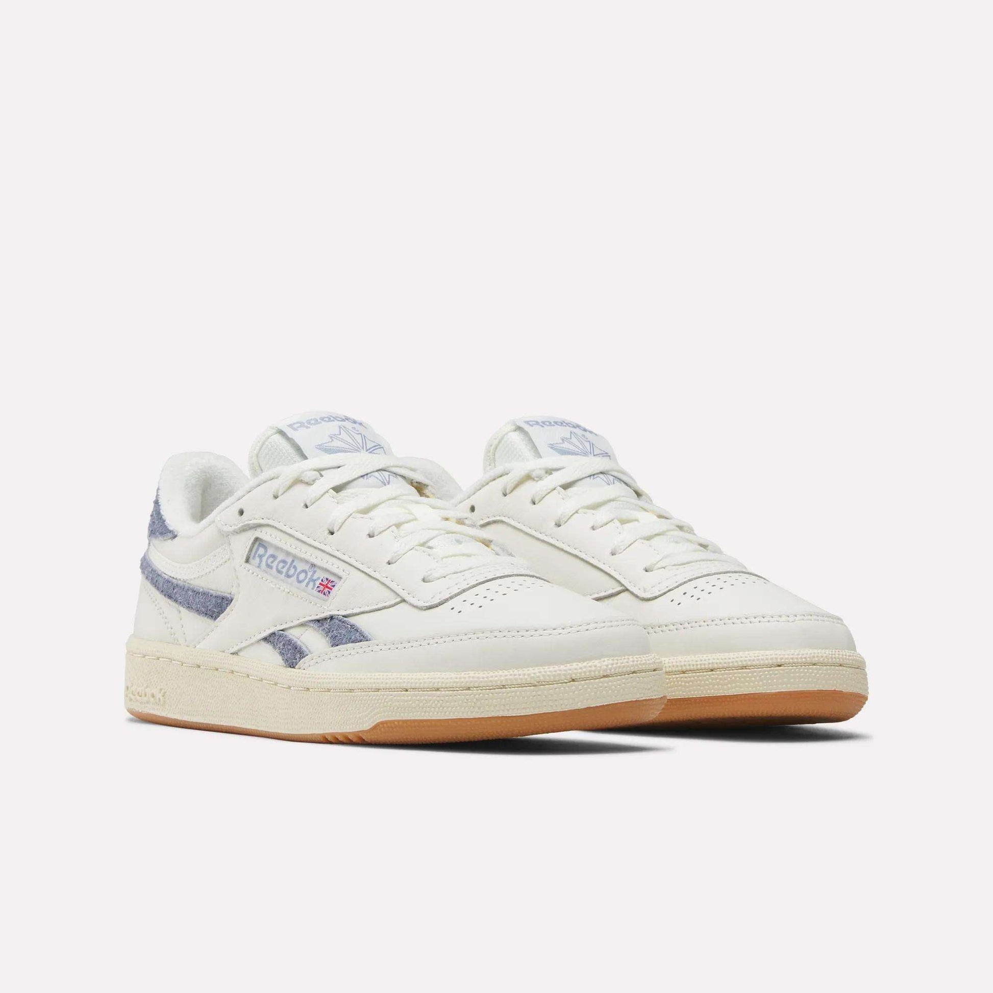 A pair of Women's Club C Revenge Shoes by Reebok, featuring white uppers, light beige soles, blue striped accents, and the Reebok logo on the side, displayed against a plain white background.