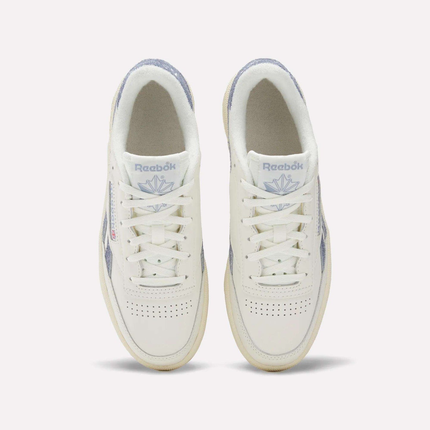 A top view of Reebok Women's Club C Revenge Shoes shows white sneakers with light purple accents, perforated toe boxes, and the Reebok logo with a purple emblem on the tongues.
