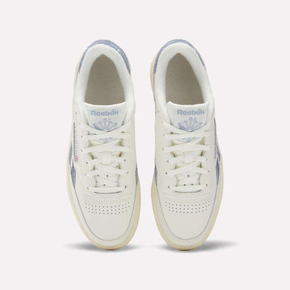 A top view of Reebok Women's Club C Revenge Shoes shows white sneakers with light purple accents, perforated toe boxes, and the Reebok logo with a purple emblem on the tongues.