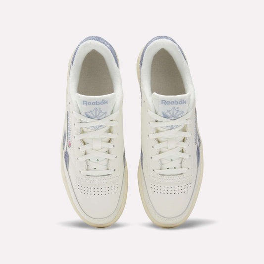 A top view of Reebok Women's Club C Revenge Shoes shows white sneakers with light purple accents, perforated toe boxes, and the Reebok logo with a purple emblem on the tongues.