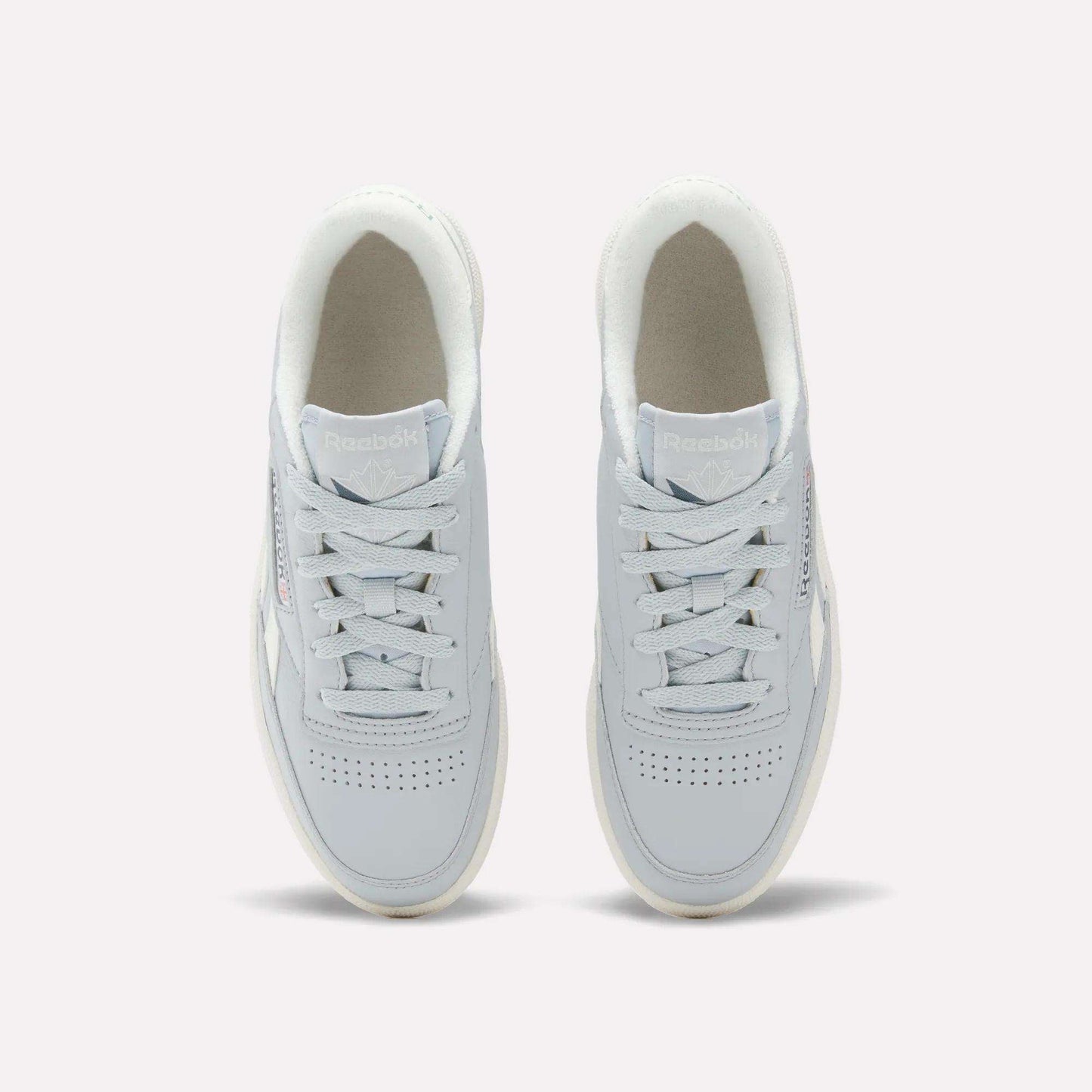 Top view of a pair of Reebok Women's Club C Revenge Shoes in light gray, featuring white soles and laces, placed side by side on a plain background. These casual shoes showcase vintage court style for a timeless look.