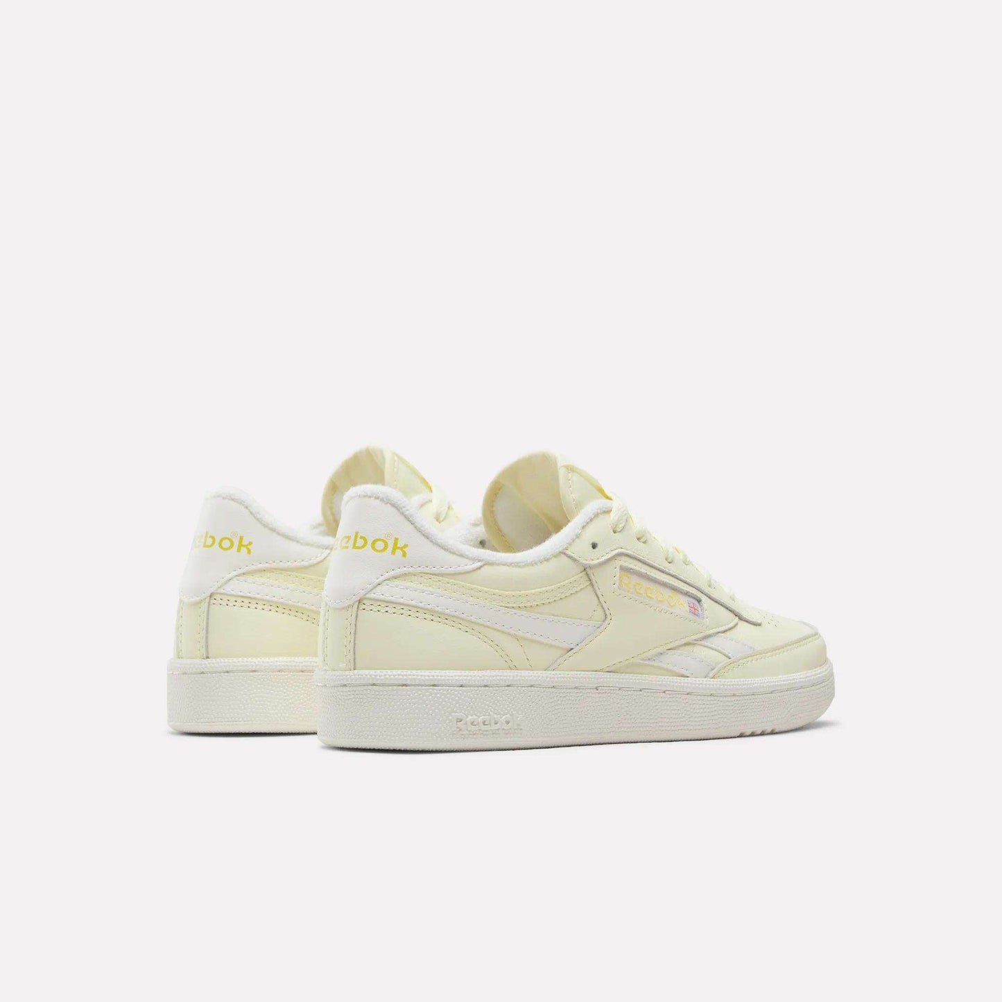 A pair of Women's Club C Revenge Shoes by Reebok in pale yellow with white soles, seen from the side and back against a plain white background. Featuring vintage court-inspired style, these casual shoes for women combine classic design with everyday comfort.