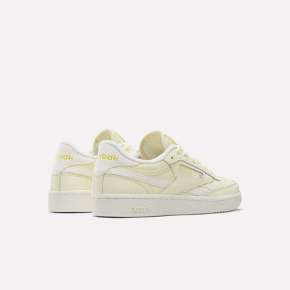 A pair of Women's Club C Revenge Shoes by Reebok in pale yellow with white soles, seen from the side and back against a plain white background. Featuring vintage court-inspired style, these casual shoes for women combine classic design with everyday comfort.