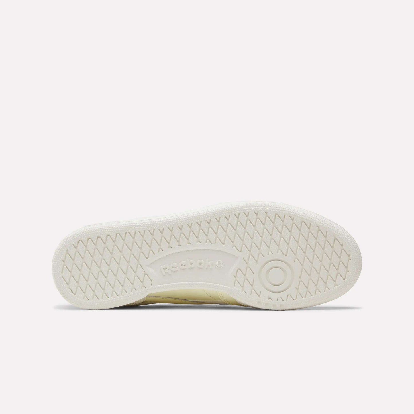 The image displays the bottom view of the Women's Club C Revenge Shoes by Reebok in a cream color, featuring a herringbone tread pattern and the Reebok logo at the center, perfectly capturing its vintage court style.