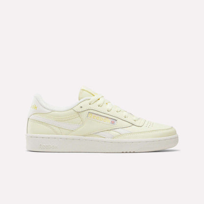 A side view of the Reebok Women's Club C Revenge Shoes is shown in Raw Yellow/Chalk/Raw Yellow, featuring pale yellow uppers with white accents, a white sole, and the Reebok logo in yellow and pastel hues on the side. Set against a plain white background, these women’s shoes highlight their vintage court-inspired style.