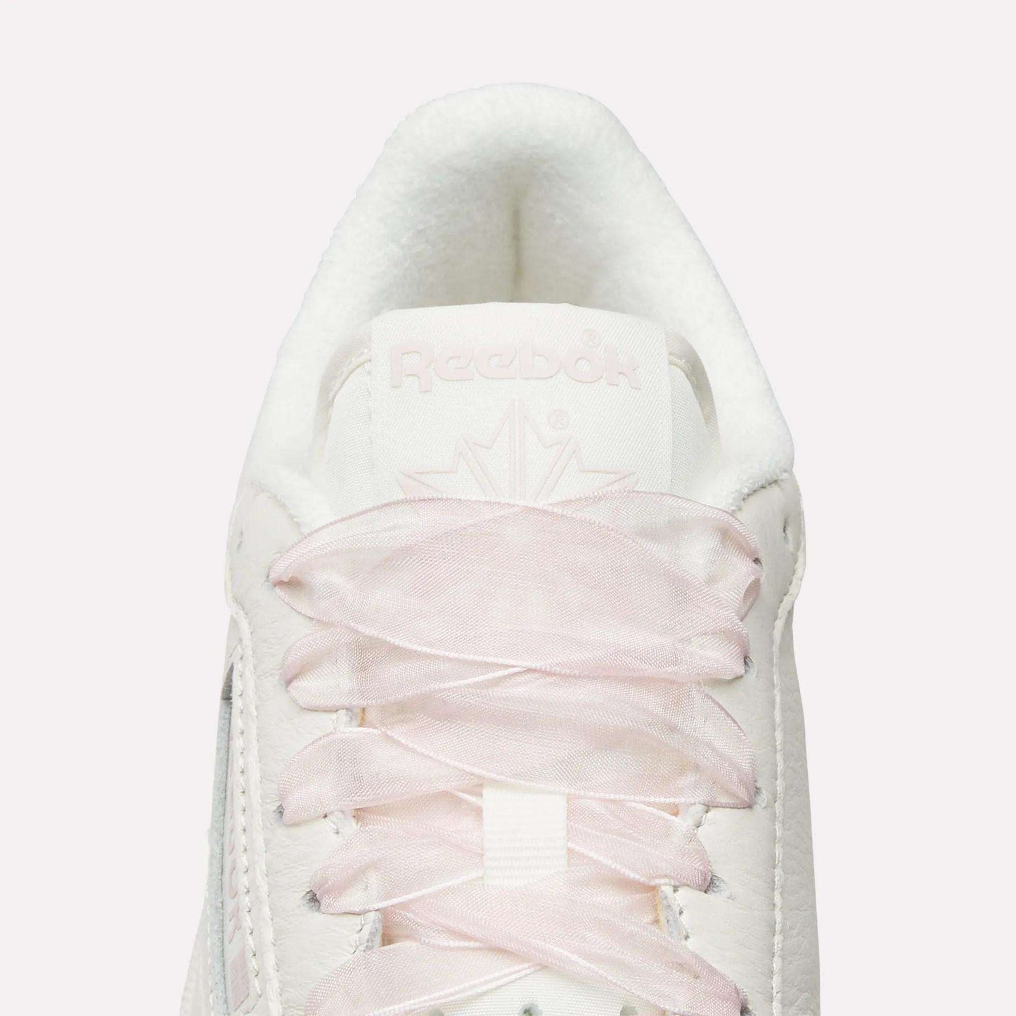 Top view close-up of Reebok Women's Club C 85 Vintage Shoes in white, featuring light pink laces, a white tongue, embossed Reebok branding, and a subtle maple leaf design for a vintage-inspired look.