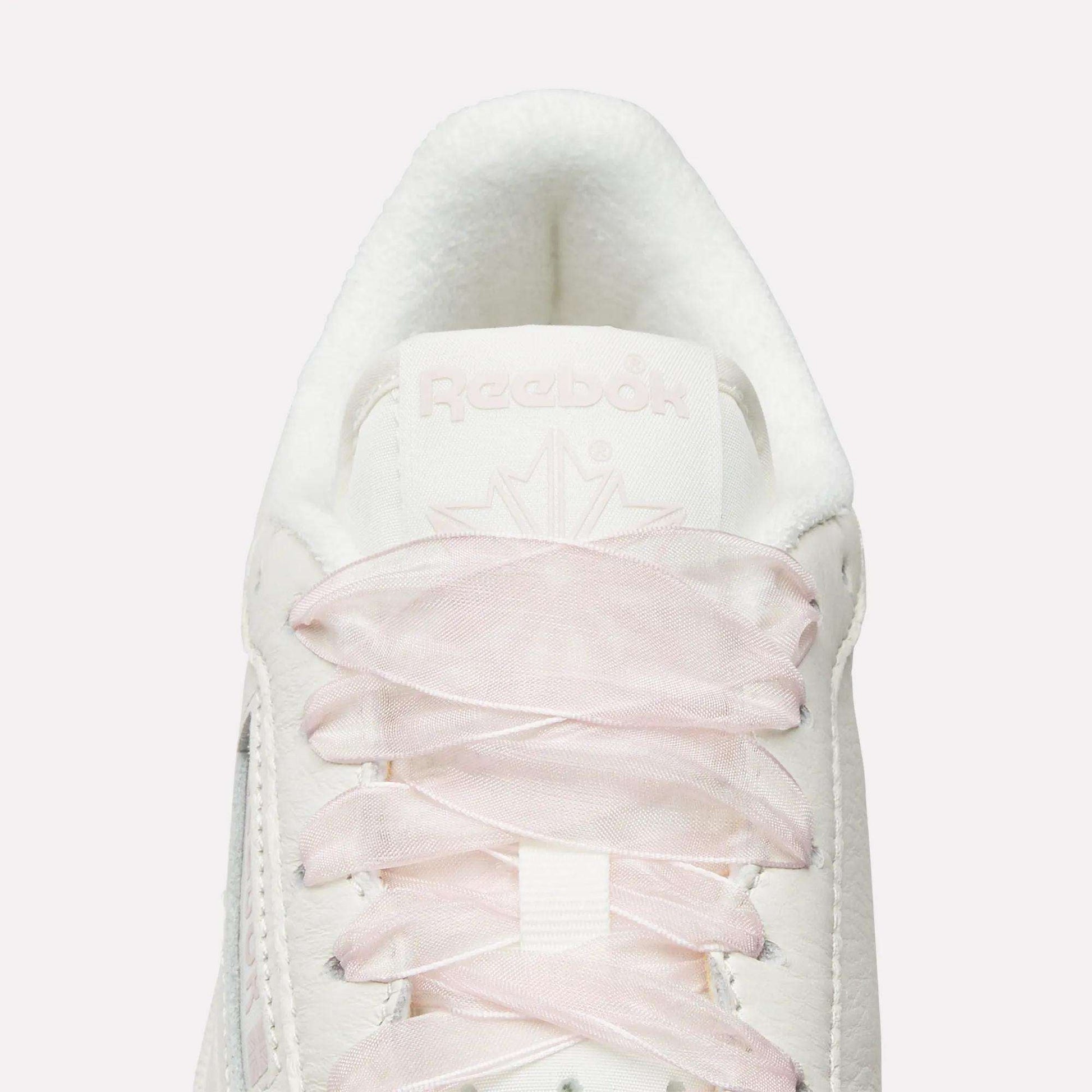 Top view close-up of Reebok Women's Club C 85 Vintage Shoes in white, featuring light pink laces, a white tongue, embossed Reebok branding, and a subtle maple leaf design for a vintage-inspired look.