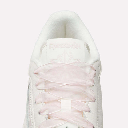 Top view close-up of Reebok Women's Club C 85 Vintage Shoes in white, featuring light pink laces, a white tongue, embossed Reebok branding, and a subtle maple leaf design for a vintage-inspired look.