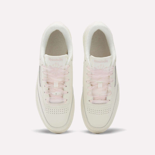 Top view of Women's Club C 85 Vintage Shoes by Reebok—white leather shoes with light pink translucent laces, perforated toe boxes, and subtle branding on the tongues, arranged side by side for a clean vintage look.