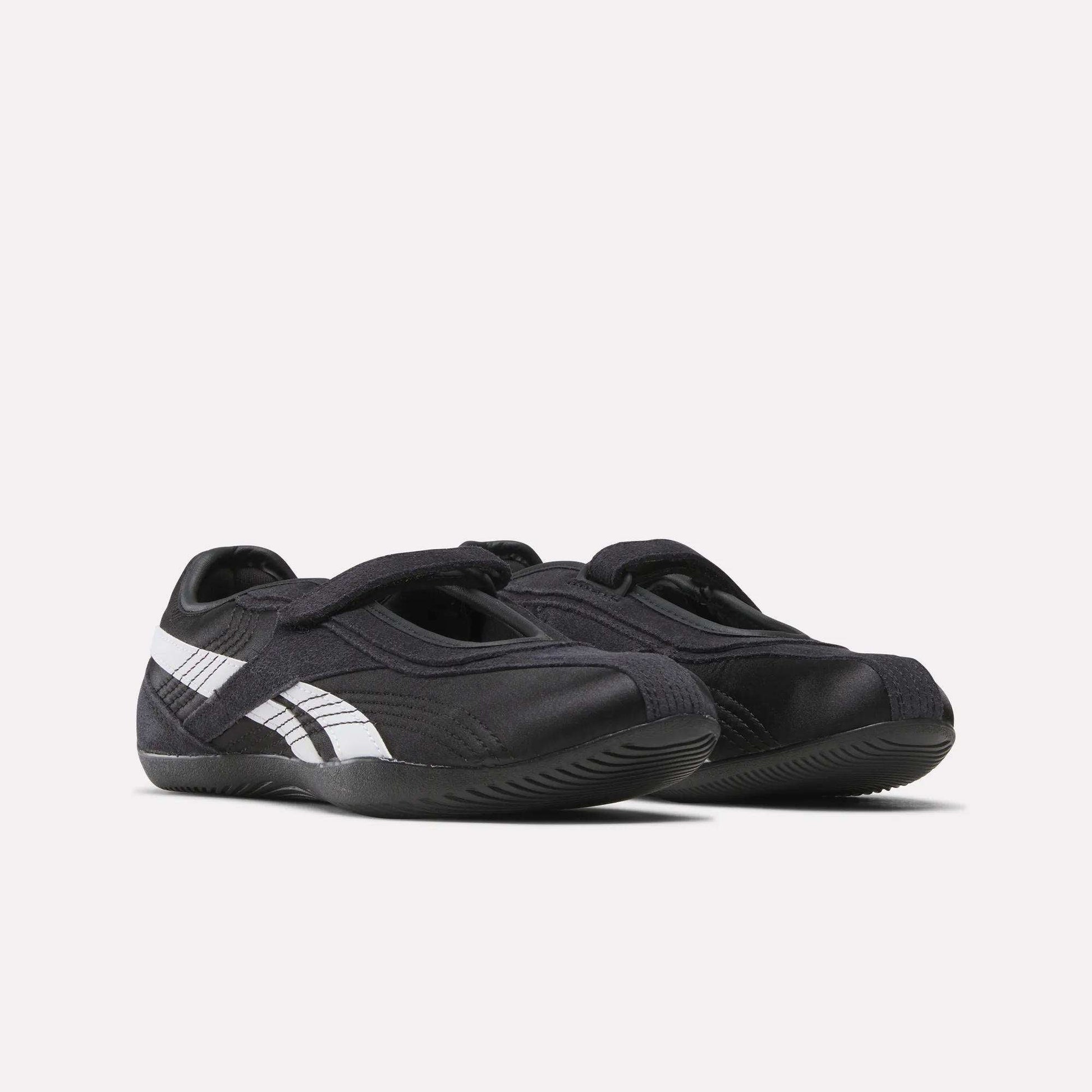 A pair of Women's Ultra Lo Mary Jane Shoes by Reebok, black with white stripes and Velcro straps, styled as low-profile runners and displayed side by side on a plain white background.