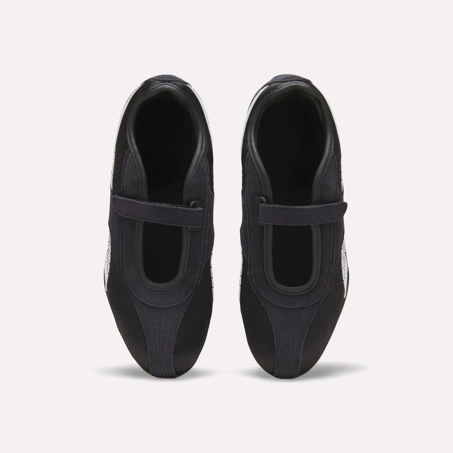 Top view of Reebok Women's Ultra Lo Mary Jane Shoes in black, featuring a single velcro strap on each, displayed side by side on a plain white background.