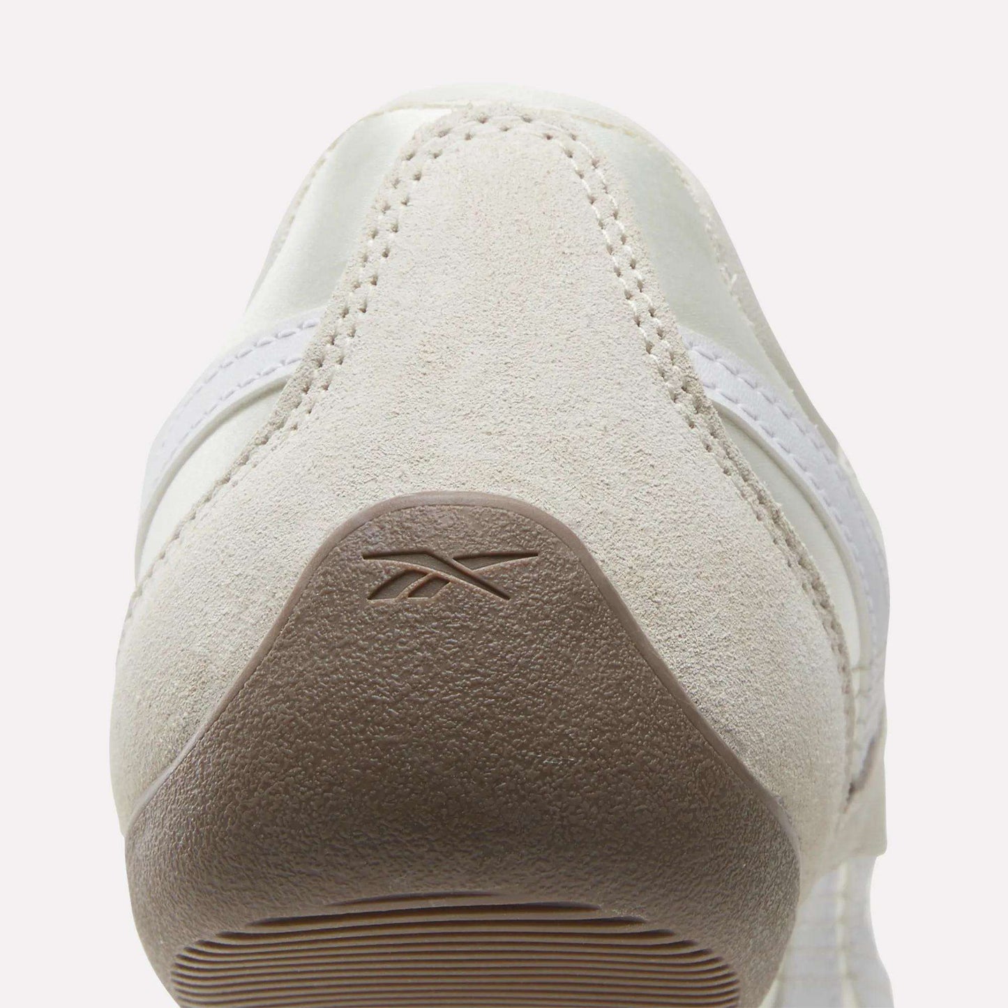 Rear view of a beige suede Women's Ultra Lo Mary Jane Shoe by Reebok, featuring a light brown textured heel with an embossed logo, white stitching, and a partial white side stripe.