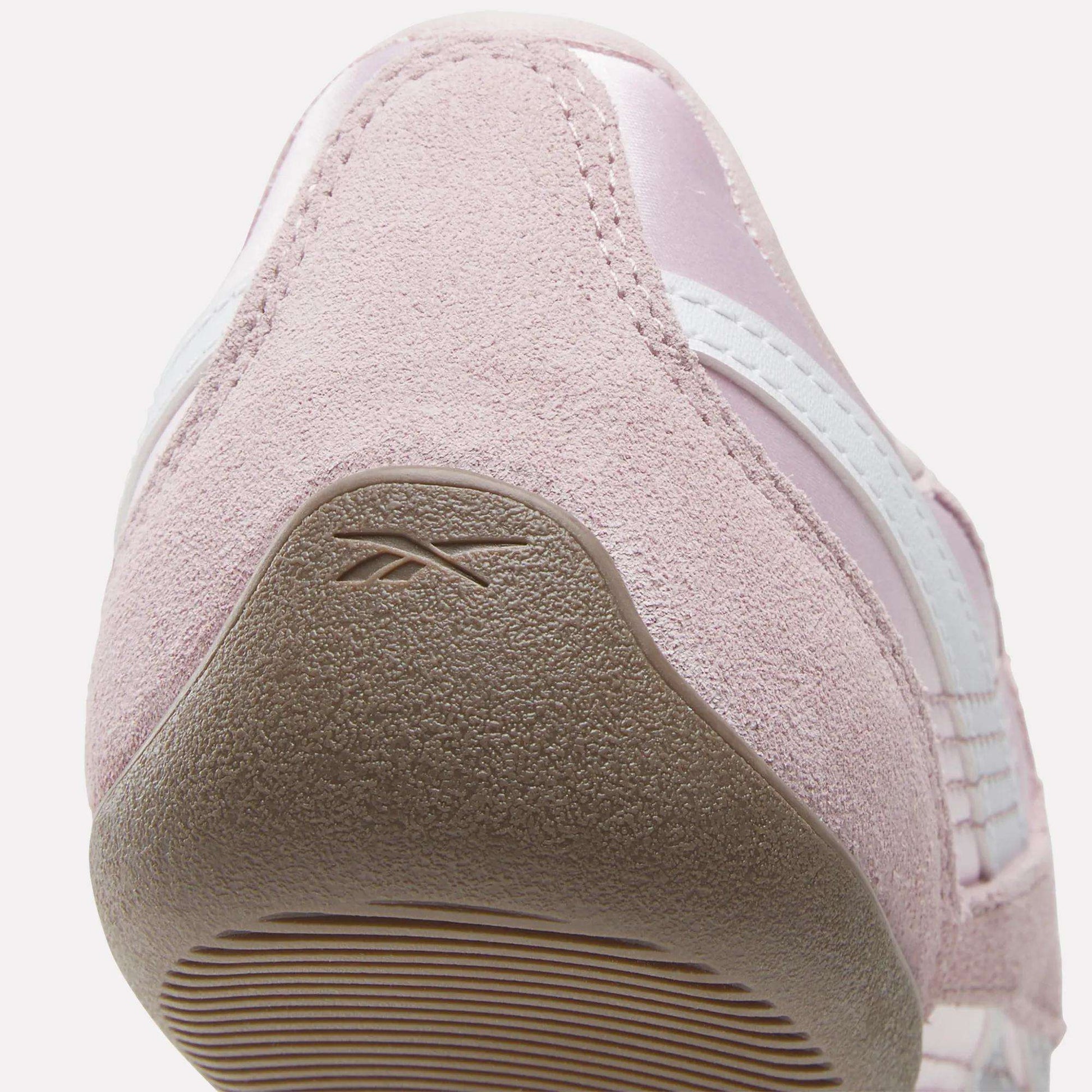 Close-up view of the heel of a light pink Women's Ultra Lo Mary Jane Shoe by Reebok, featuring a textured suede finish, white stripes, and the Reebok logo embossed on the heel section of the rubber outsole.