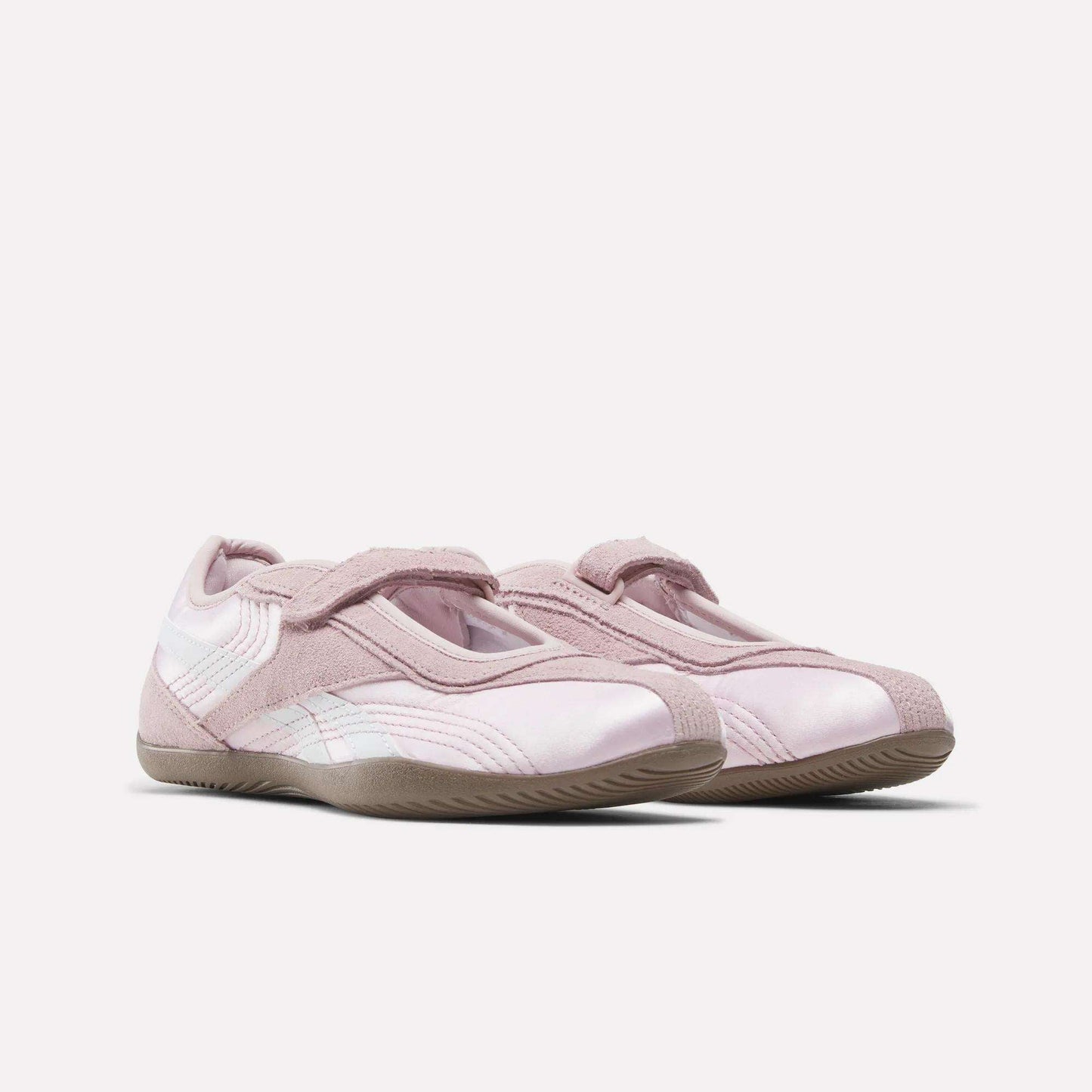 The Women's Ultra Lo Mary Jane Shoes by Reebok feature a light pink low-profile runner style with suede and mesh accents, velcro straps, and textured rubber soles, shown on a plain white background.