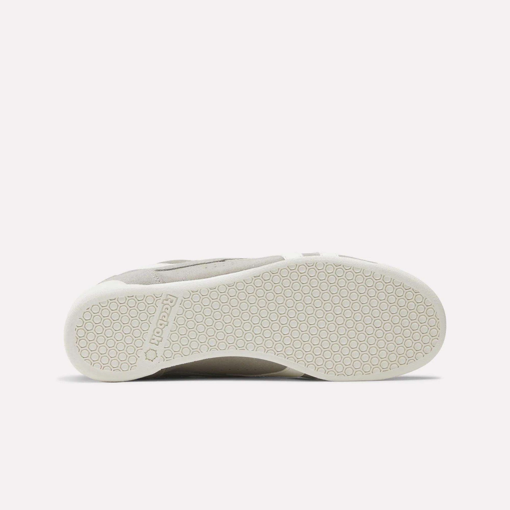 A Women's Freestyle Lo Shoe by Reebok lies on its side, highlighting the textured, hexagon-patterned rubber sole with a Reebok logo near the heel. This retro sneaker stands out against a plain white background.