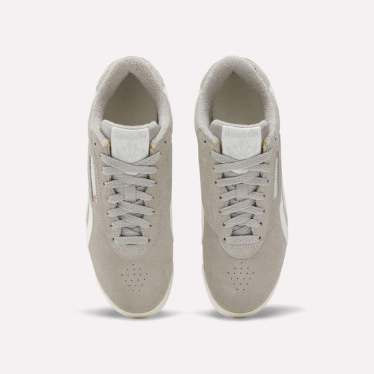 Top view of Reebok Women's Freestyle Lo Shoes in light grey with white soles, matching laces, and Reebok logos on the tongue and side, featuring a retro sneakers vibe against a plain white background.