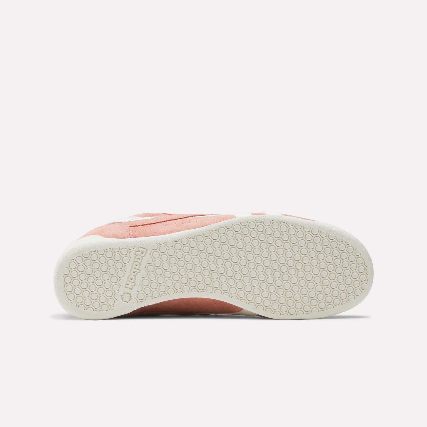 The Reebok Women's Freestyle Lo Shoes in pink and white feature a retro sneaker design, shown from the side to highlight the textured white rubber sole with a hexagonal pattern.