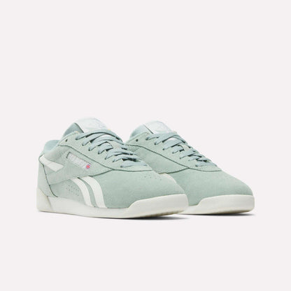The Reebok Women's Freestyle Lo Shoes in light green suede feature white accents, soles, and side stripes, plus a subtle red logo tag near the laces. The retro sneakers are shown on a plain white background.