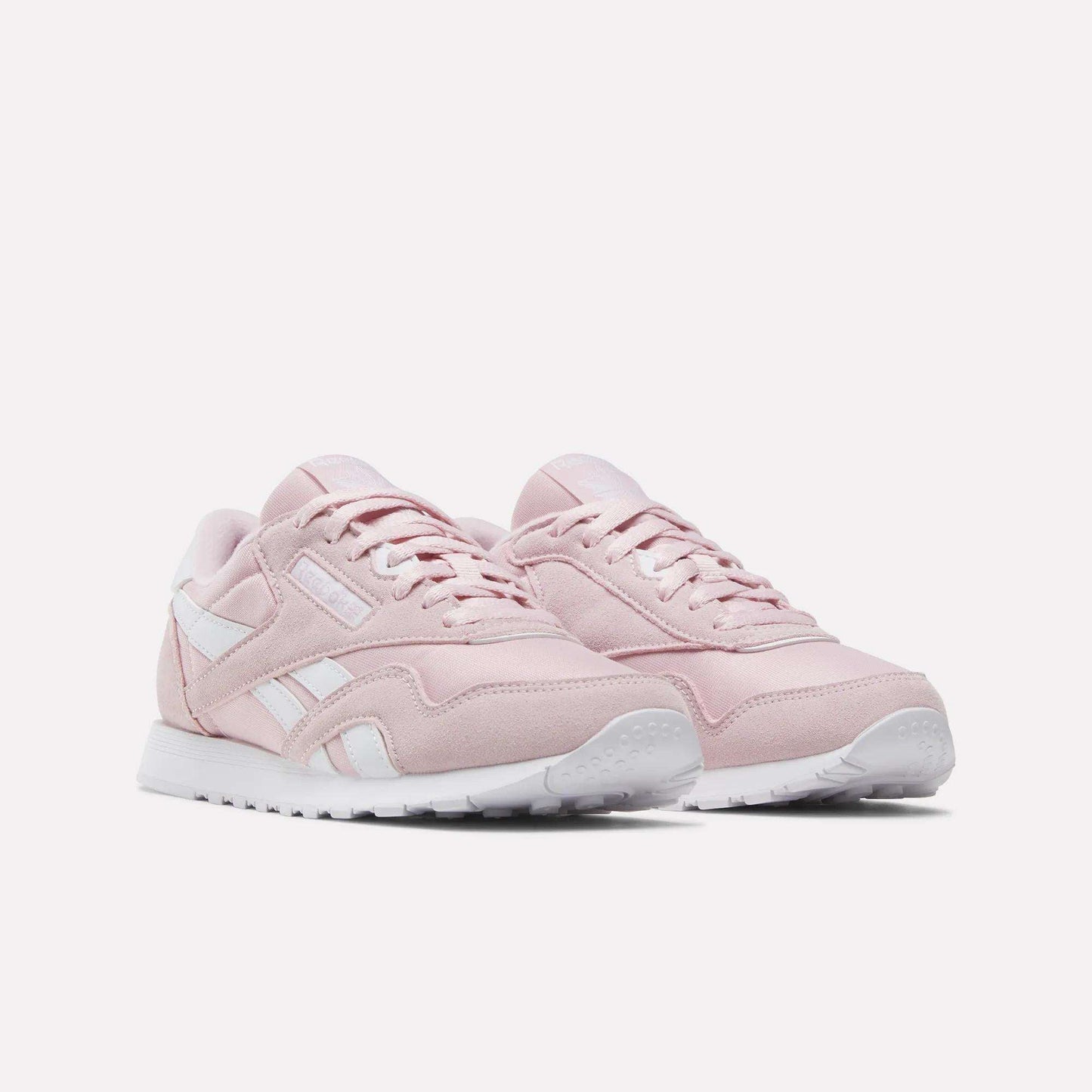 A pair of Women's Classic Nylon Shoes by Reebok in light pink, featuring white soles and white Reebok logo accents, displayed on a plain white background.