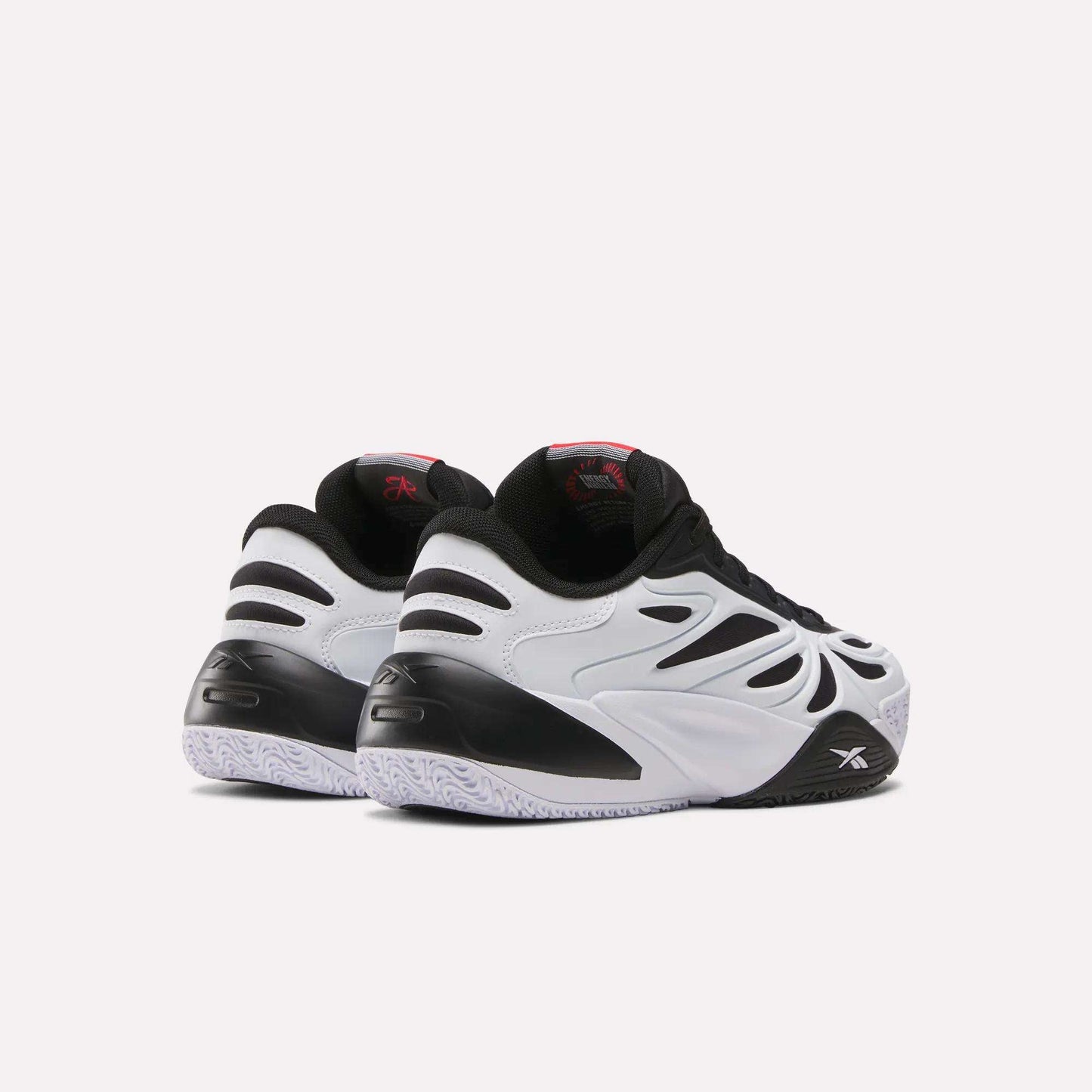 The Reebok Angel Reese 1 Shoes for big kids, featuring black and white wavy designs, black accents, and textured white soles, are displayed from the back and side on a plain light background.