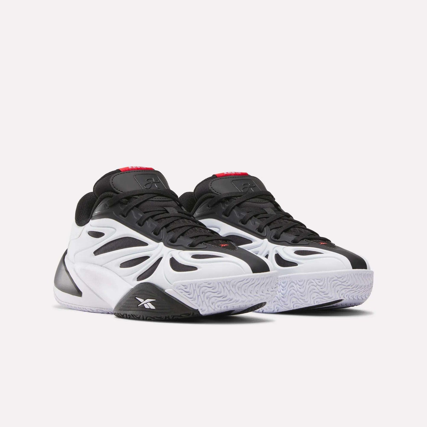 The Reebok Angel Reese 1 Shoes - Big Kids feature a bold, futuristic black and white design with black accents, a chunky sole, and red tongue details, inspired by Angel Reese shoes and displayed on a plain white background.