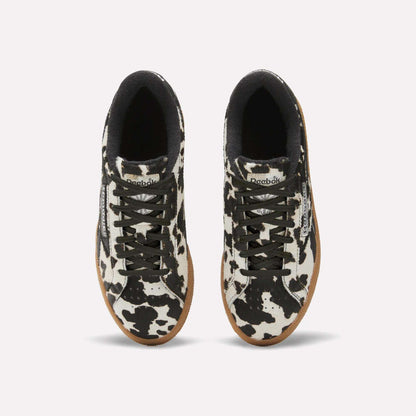 Top view of Reebok Women's Club C Grounds UK Shoes with black and white cow print uppers, black laces, black inner lining, white midsoles, and tan rubber outsoles on a plain white background.