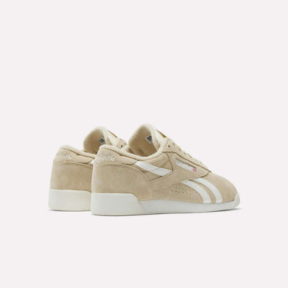 The Reebok Women's Freestyle Lo Shoes feature beige suede uppers, white side stripes, and rubber soles, shown from the back and side on a plain white background.