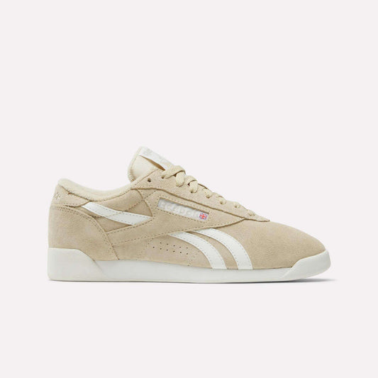 The Women's Freestyle Lo Shoes by Reebok feature beige suede, white stripes, a white sole, and beige laces. Displayed in a side profile on a plain white background, they capture the classic retro sneaker style.