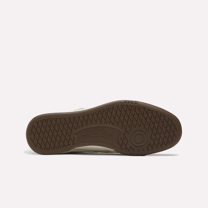 The image displays the brown rubber sole of the Reebok Club C Revenge Vintage Shoes, highlighting a textured grip pattern, iconic Reebok branding, and a circular design near the heel that pays homage to classic tennis-inspired footwear.