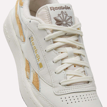 Close-up of the Reebok Club C Revenge Vintage Shoes, featuring a crisp white leather upper accented with tan and gold details. The shoe showcases the iconic Reebok logo alongside a maple leaf design on the tongue, while white laces threaded through the eyelets emphasize its classic tennis-inspired aesthetic.