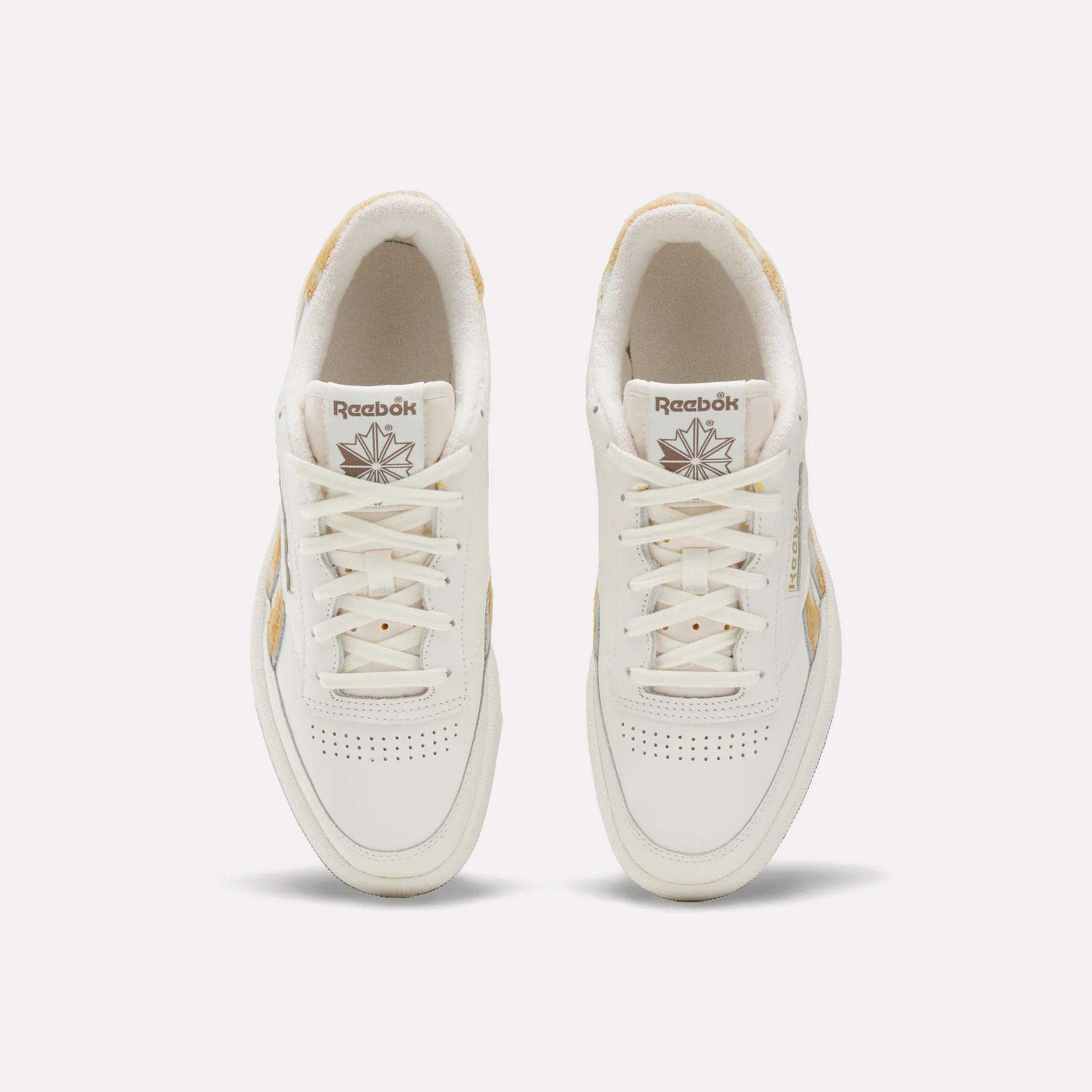 Top view of a pair of Reebok Club C Revenge Vintage Shoes with beige accents, white laces, and perforated detailing on the toes, featuring a classic leather upper. These tennis-inspired sneakers are displayed on a plain light background.