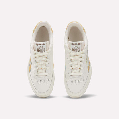 Top view of a pair of Reebok Club C Revenge Vintage Shoes with beige accents, white laces, and perforated detailing on the toes, featuring a classic leather upper. These tennis-inspired sneakers are displayed on a plain light background.