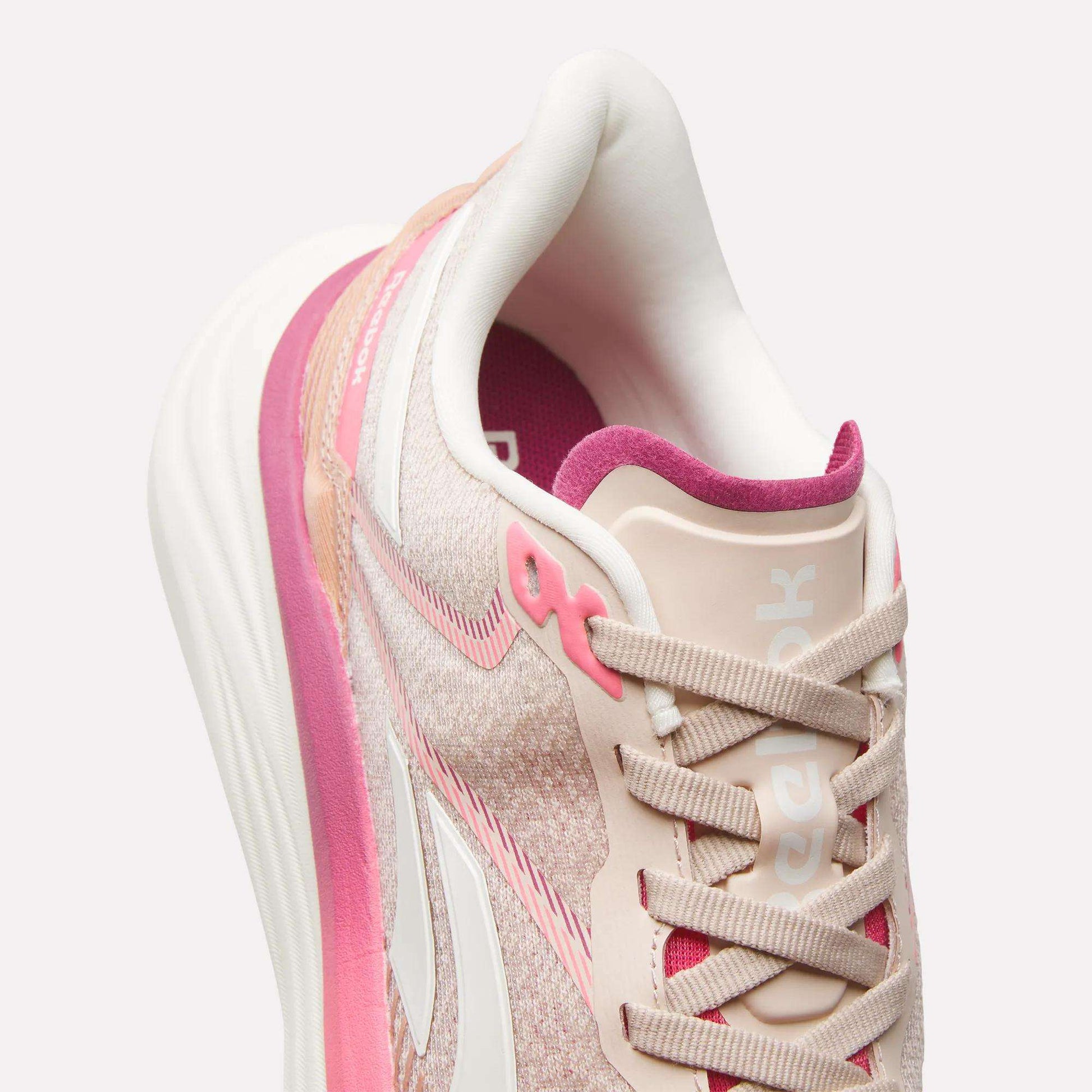 A close-up, angled view of the Reebok Women's Viva Speed Shoes in pink and beige with white accents, a pink inner lining, and white laces highlights their cushioned design and comfortable materials.