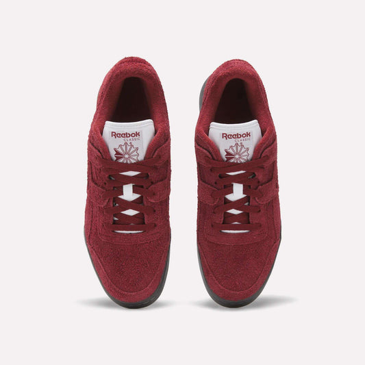 A pair of red Reebok Workout Plus Shoes with white tongues, black soles, and matching red laces and logos is shown from above on a plain white background, highlighting the classic fitness style.