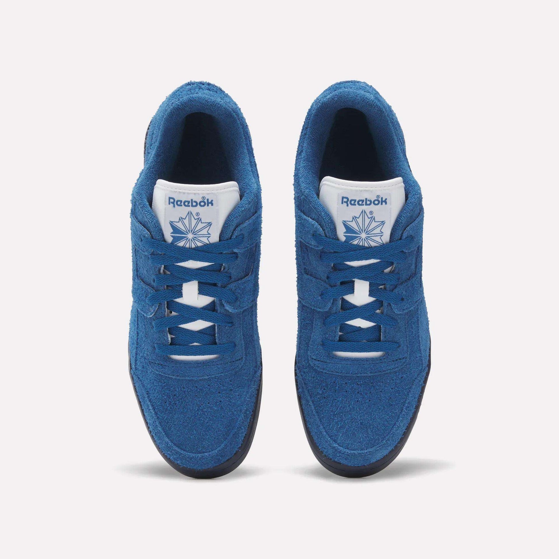 Top view of Reebok Workout Plus Shoes in blue, showing white tongues with the Reebok logo and dark outsoles, placed side by side on a white background—a classic '80s fitness style from Reebok.