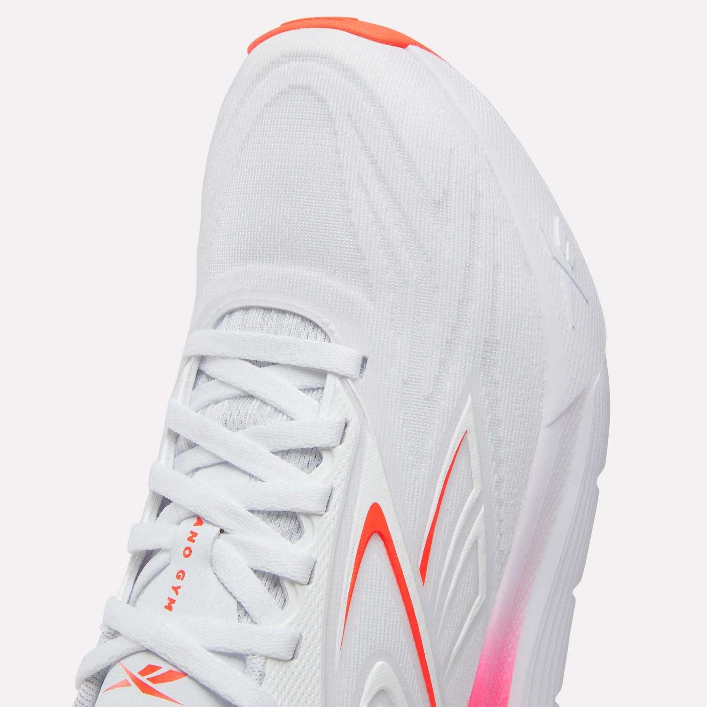 Close-up of the Reebok Women's Nano Gym 2.0 Training Shoes in white, with red and orange accents, a textured upper, white laces, cushioned sole with pink at the midsole—perfect for training.