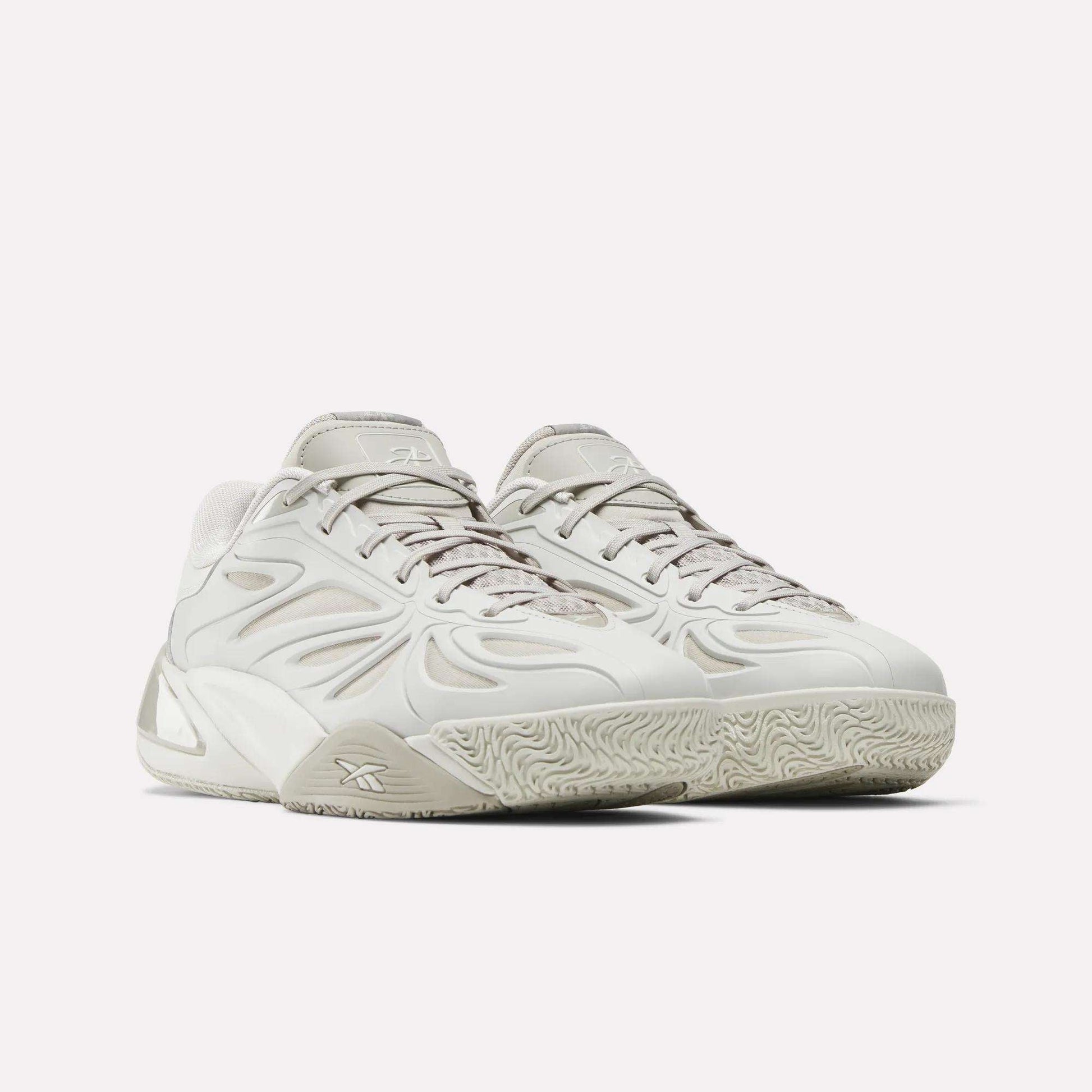 The Reebok Angel Reese 1 Basketball Shoes feature a modern design in light gray with wave-like side patterns, textured soles, and laces, inspired by Angel Reese and showcased against a plain white background.