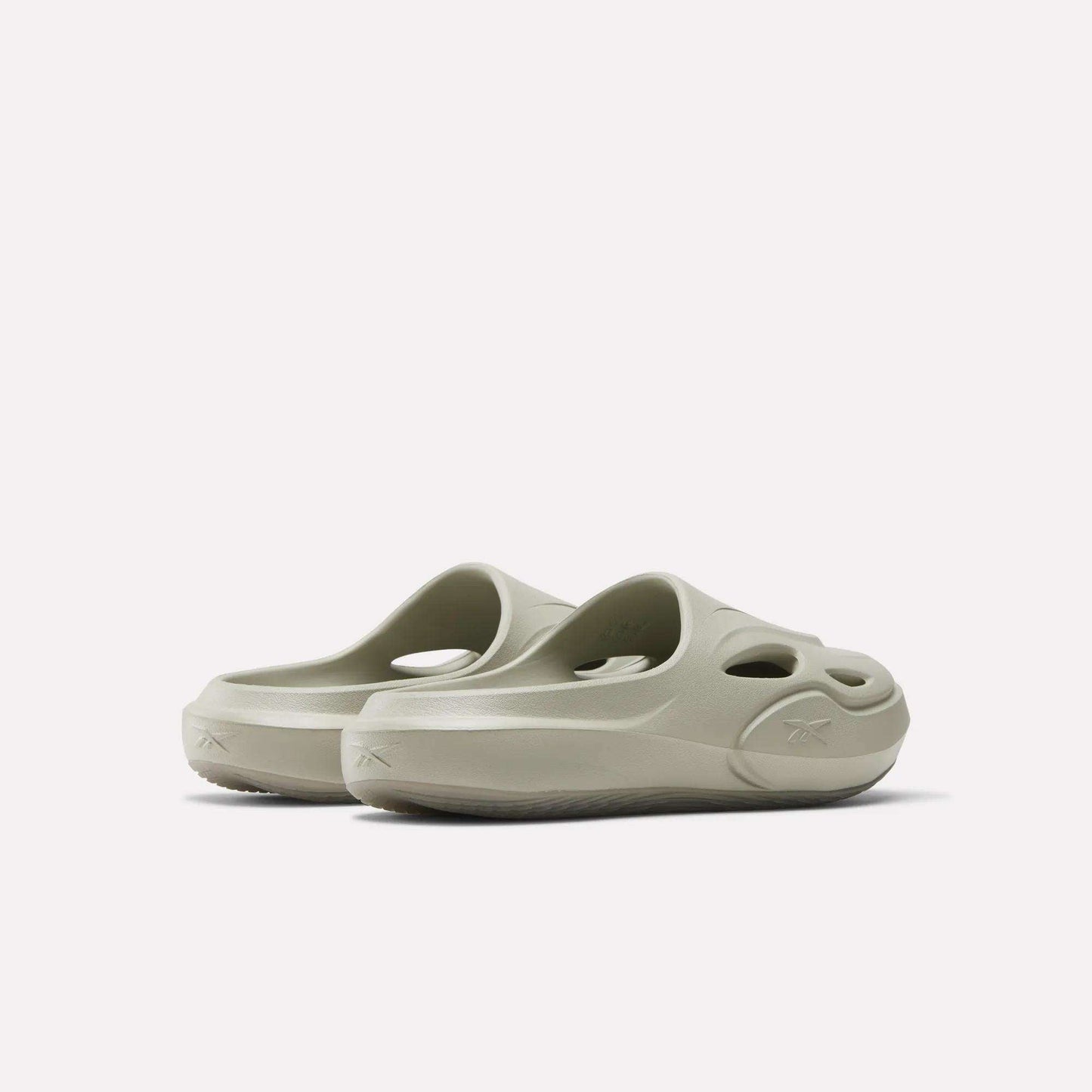 The Reebok DMX Recovery Mules are light beige slip-on EVA shoes with round cut-out holes on the upper and sides, displayed from a rear angle against a plain white background.