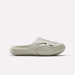 The Reebok DMX Recovery Mules are light beige slide sandals with a thick molded EVA sole, upper cutout details, and an embossed Reebok logo, shown in side profile against a plain white background.