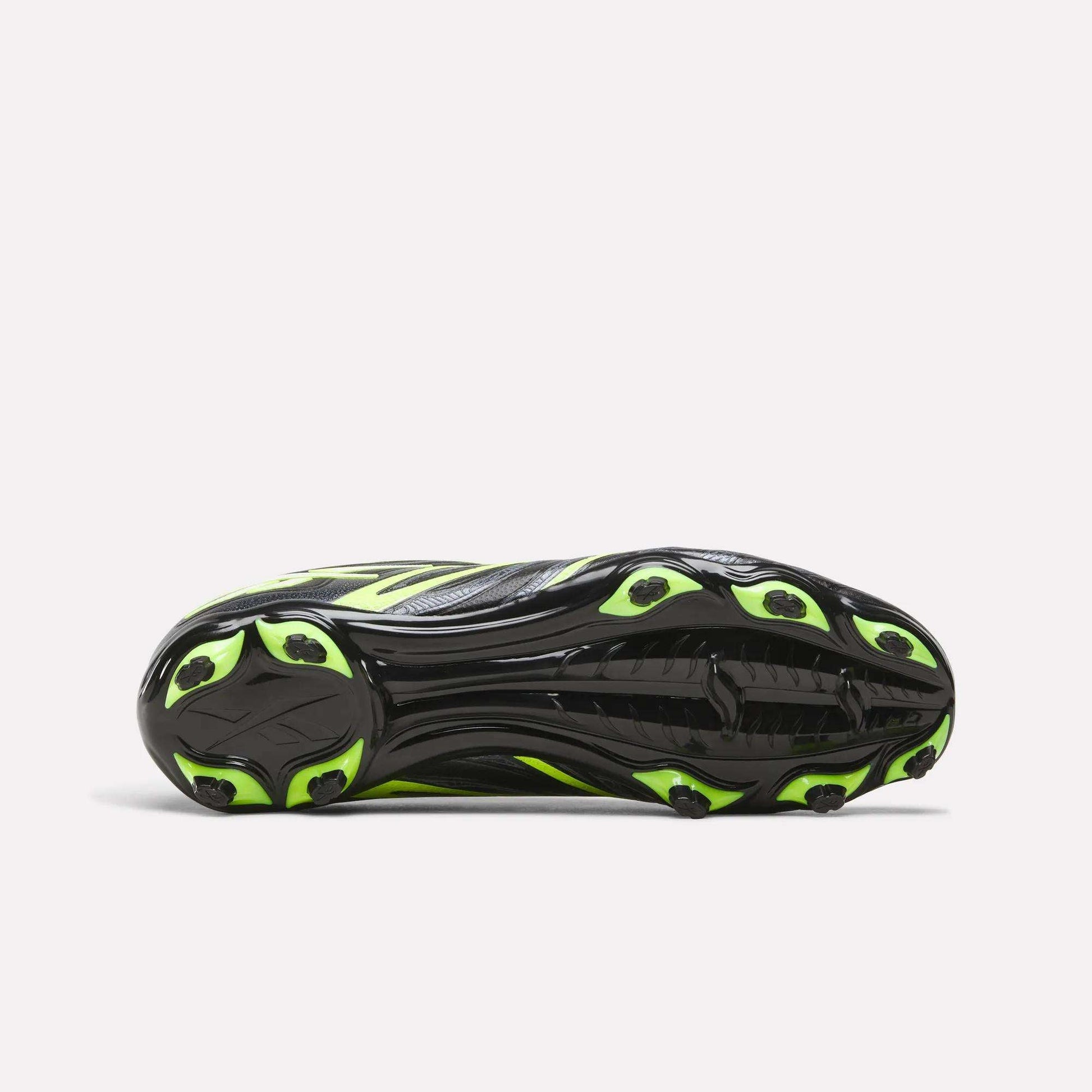 The image shows the sole of the Reebok Sidewinder 26 League FG Cleats for big kids, featuring a black base with neon yellow accents and several firm ground studs for dependable traction on the field.