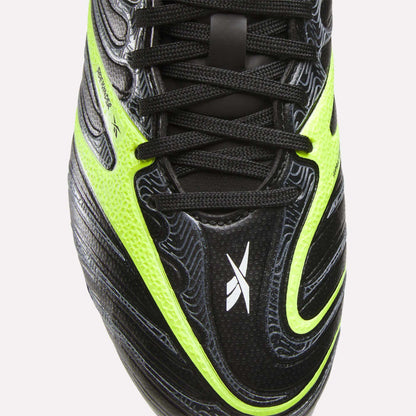 Close-up of the upper part of Reebok Sidewinder 26 League FG Cleats for big kids, featuring black color with neon yellow and white accents, black laces, textured surface, firm ground studs, and a small white X-shaped logo on the toe.