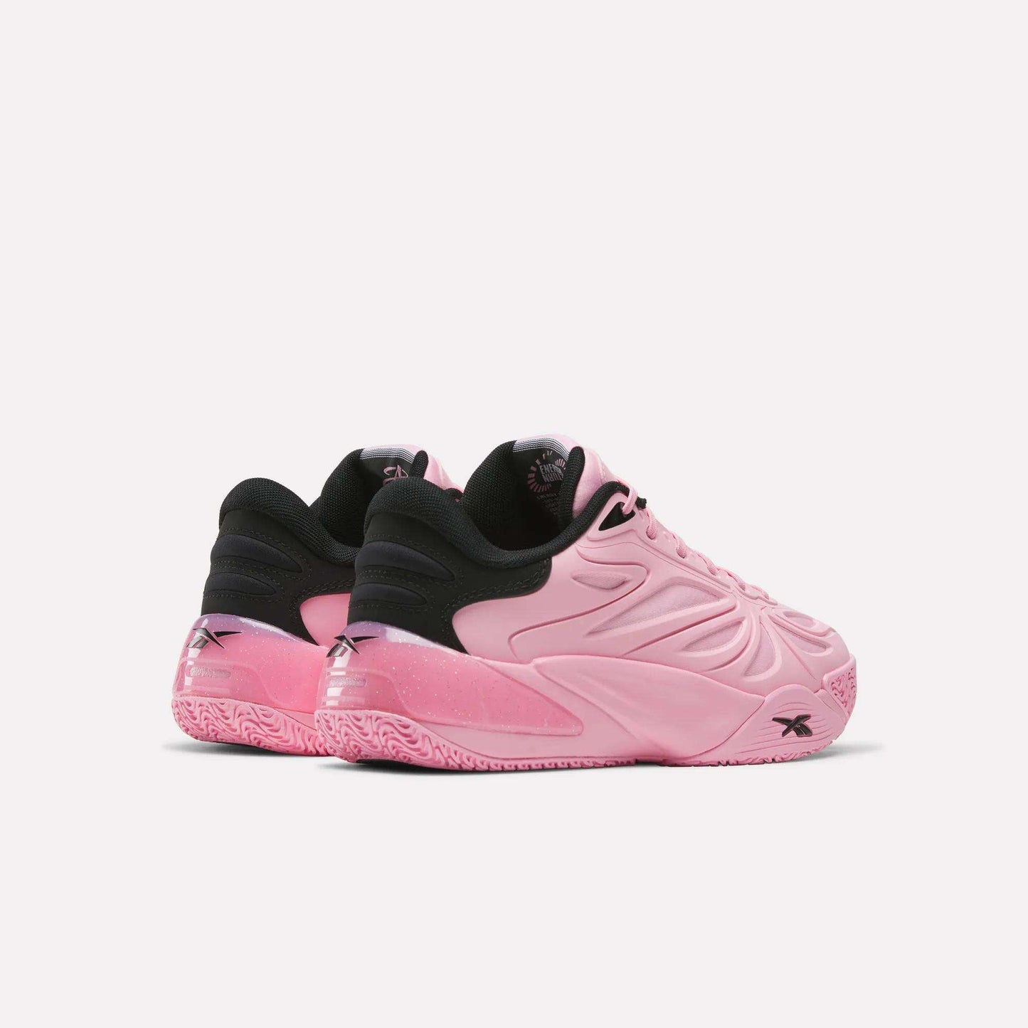 Two pink Angel Reese 1 Shoes by Reebok, featuring black inner lining and heel accents, are displayed against a plain white background. Showcasing a textured sole and wavy side patterns, these performance basketball shoes are inspired by Angel Reese and crafted to elevate your game with the advanced Reebok Energy Return System for responsive comfort on the court.