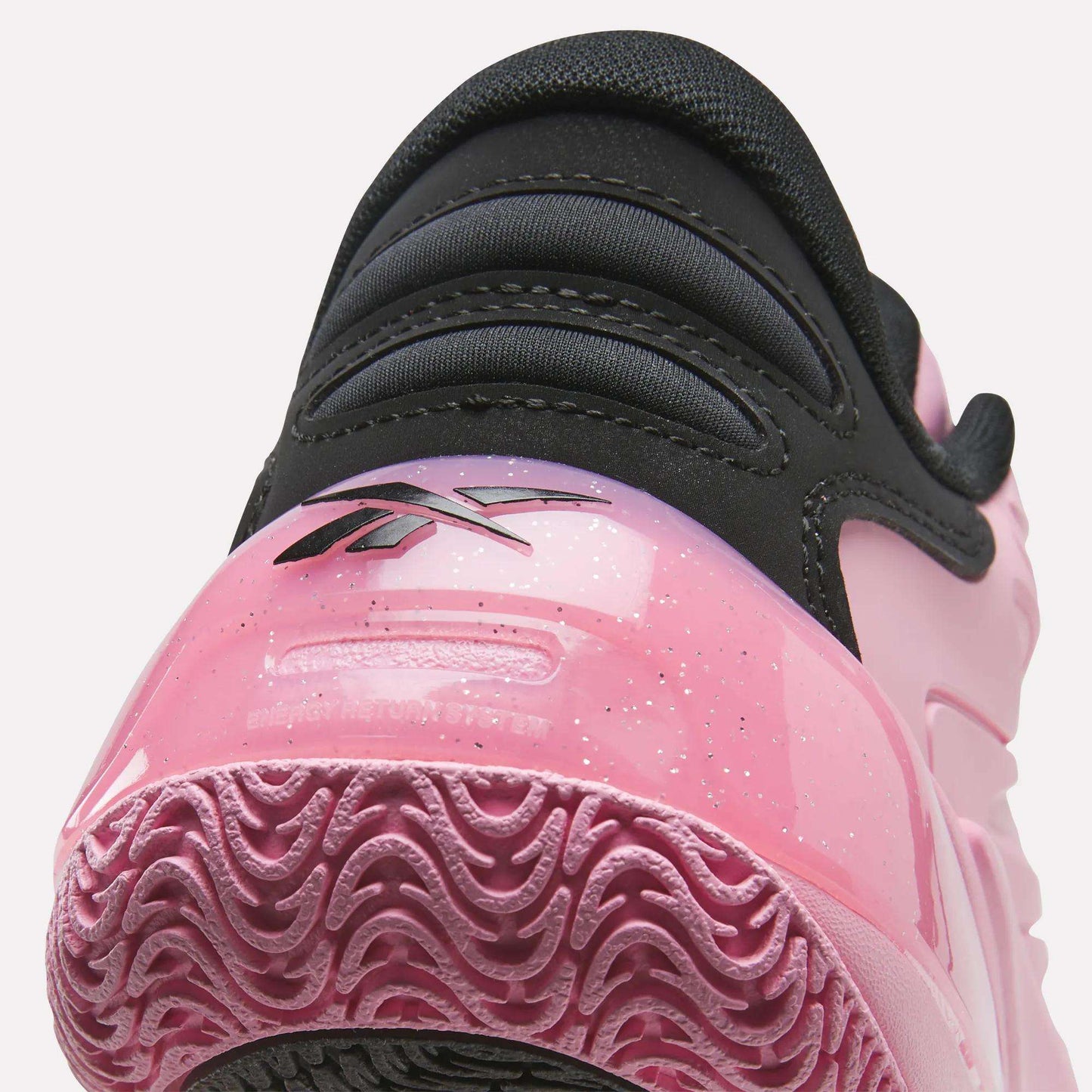 Close-up of the heel of the Angel Reese 1 Shoes by Reebok, showcasing a black upper, pink shiny heel detail with the Reebok logo, and a textured pink outsole—featuring the advanced Reebok Energy Return System inspired by performance basketball shoes.
