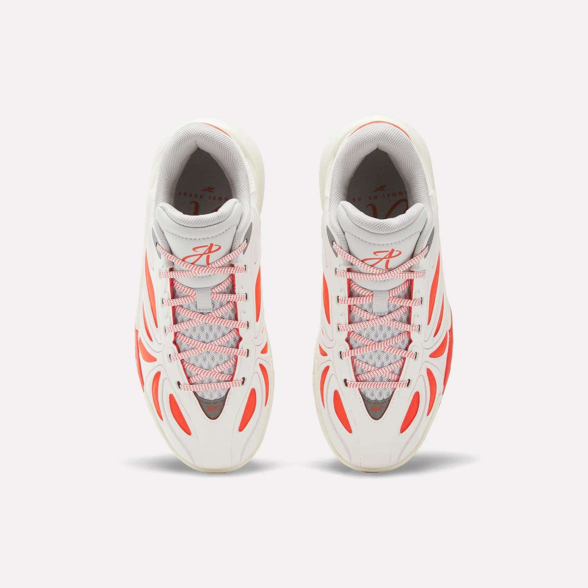 Top view of Reebok Angel Reese 1 Shoes for big kids in white with gray accents and bold orange lines and lace loops, placed side by side on a light background.