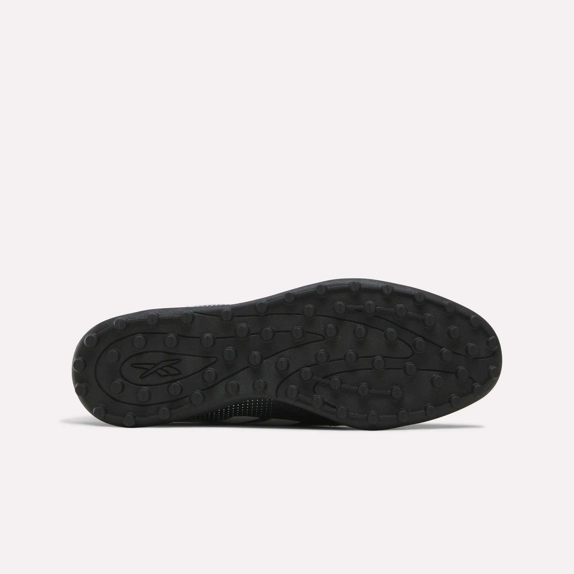 Black rubber sole featuring a textured tread pattern with small round bumps, displayed against a plain light background. Designed for the Reebok Strike Turf Soccer Shoes, this sole is perfect for soccer practice. A small Reebok logo appears on the left side of the sole.