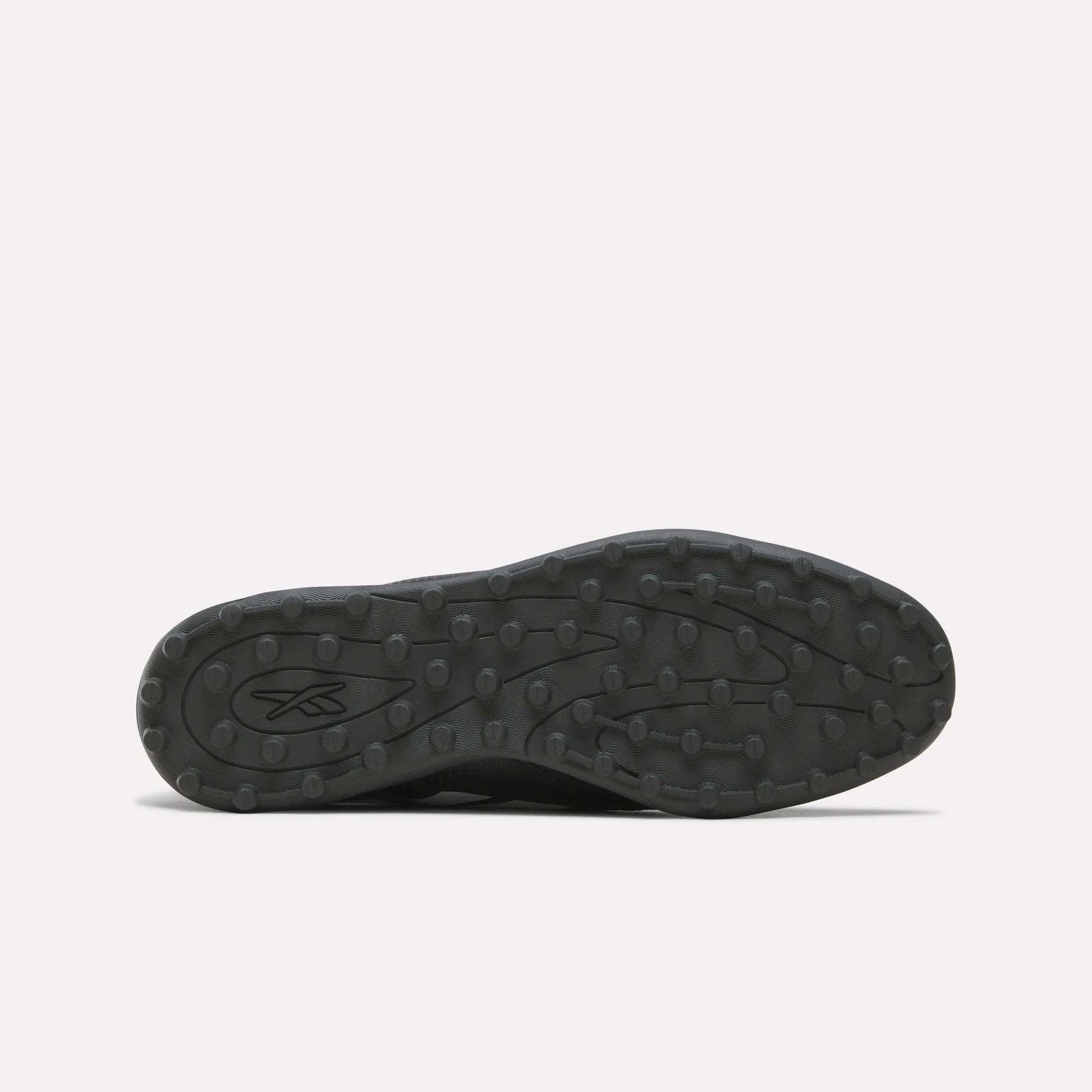 The image displays the black rubber sole of the Reebok Strike Turf Soccer Shoes, viewed from below. The sole features round traction bumps ideal for turf soccer play and practice, along with an abstract Reebok logo near the heel.