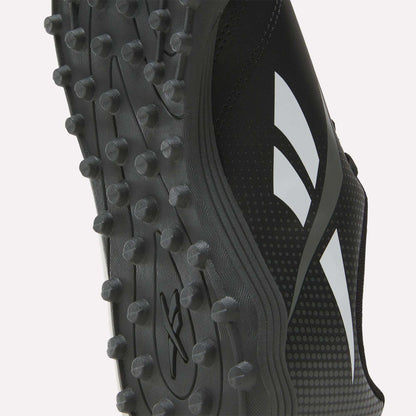 Close-up of the sole of a black Reebok Strike Turf Soccer Shoe, highlighting its rubber traction studs and white geometric Reebok logos on the side—ideal for soccer practice.